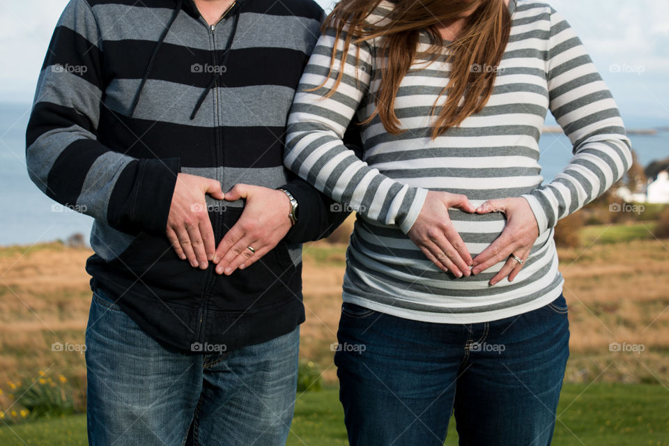 Midsection of couple making heart shape on stomach