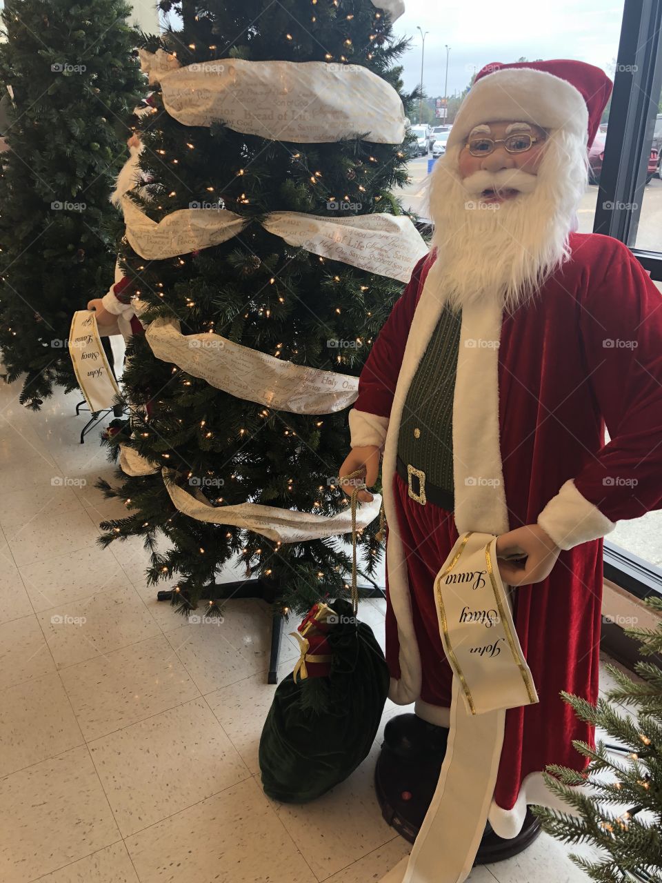 A  life size Santa figure next to a green undecorated Christmas tree. 