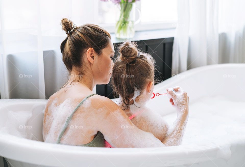 Young mother woman and little tween girl daughter having fun in bath with foam at home