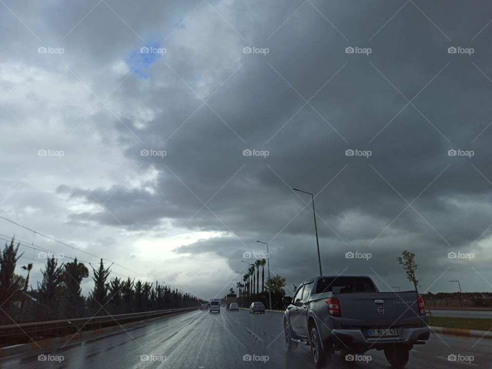 A photo of dark cloudy and stormy sky with highway and cars. From the car