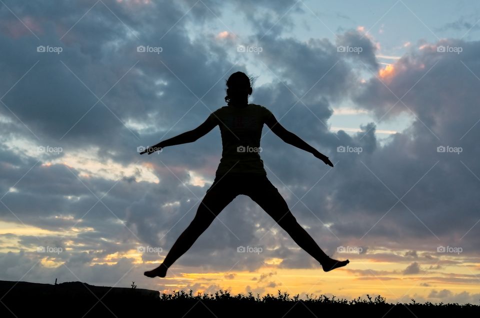 Silhouette of a girl jumping on a trampoline at sunset
