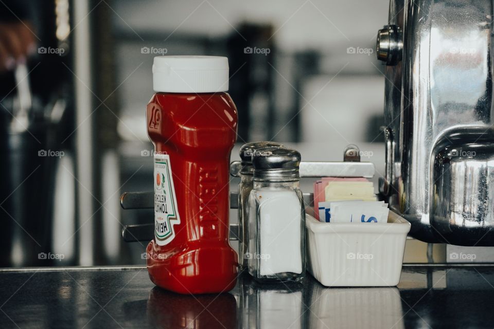 close up ketchup bottle salt pepper and sugar packets on a diner table 