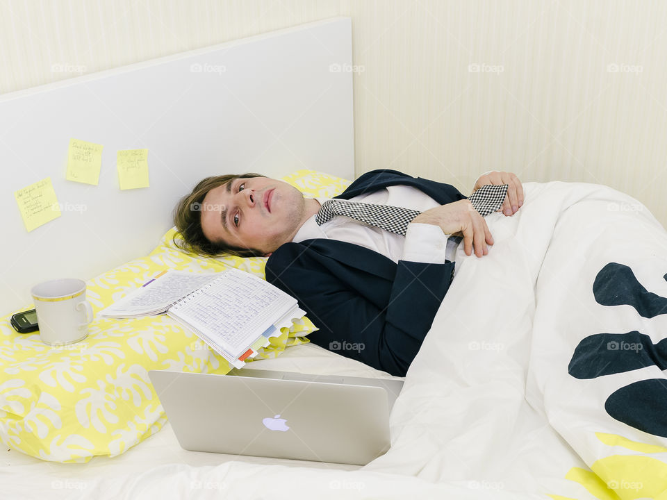 Man in bad wearing suit and tie working from home in bed, joke