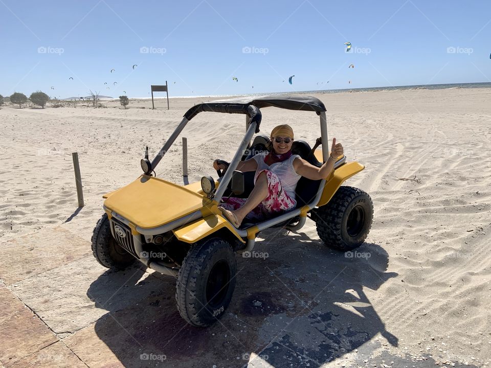 Happy mature woman driving mini buggy in the beach 