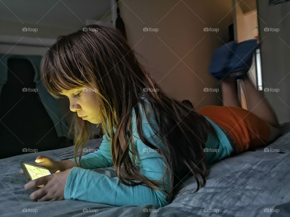 Girl playing on cellphone in dark on bed