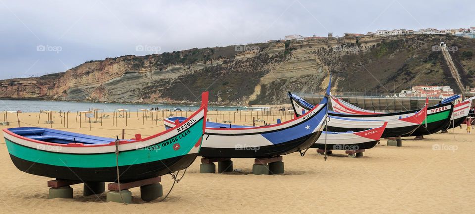 Brightly coloured, wooden fishing boats sit on the sand at Praia Da Nazaré, Portugal 