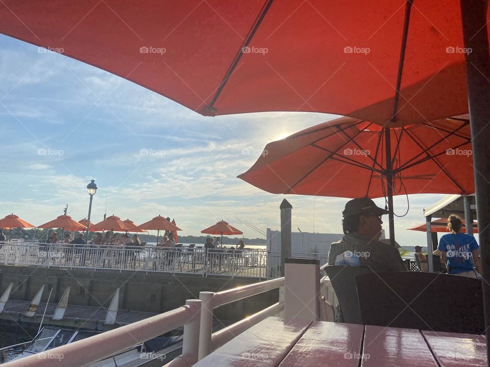 People enjoying food, drink, music, friends, sunshine and a view of the water under the orange umbrellas at an outdoor bar on the 9th Avenue Pier in Belmar, NJ. If you come here on a nice day, you never want to leave! Good vibes on the bay!