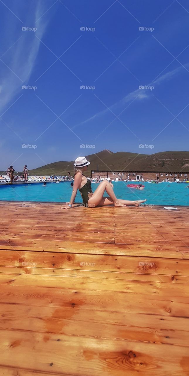 девушка в шляпе сидит у бассейна на деревянном полу