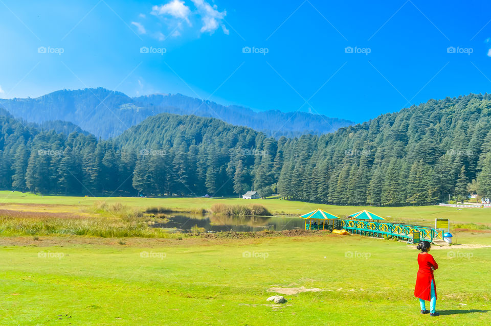 A woman in red dress turns back stands on a meadow in a hill station of India in springtime. Vacation Concept