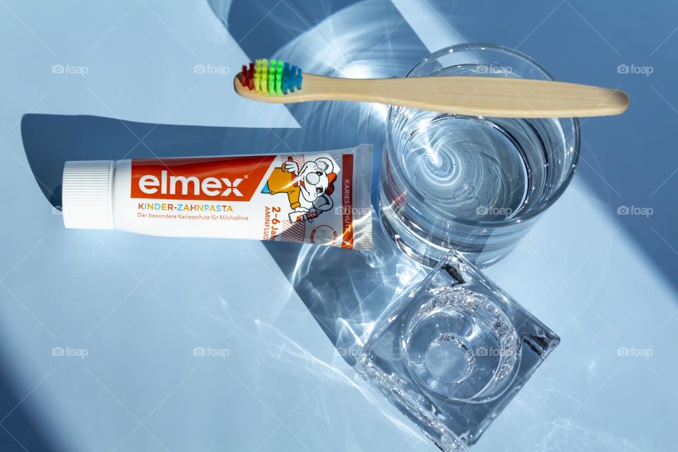 Elmex toothpaste for small children for oral and dental care, ecological toothbrush is on a blue background, with water, and a green flower.