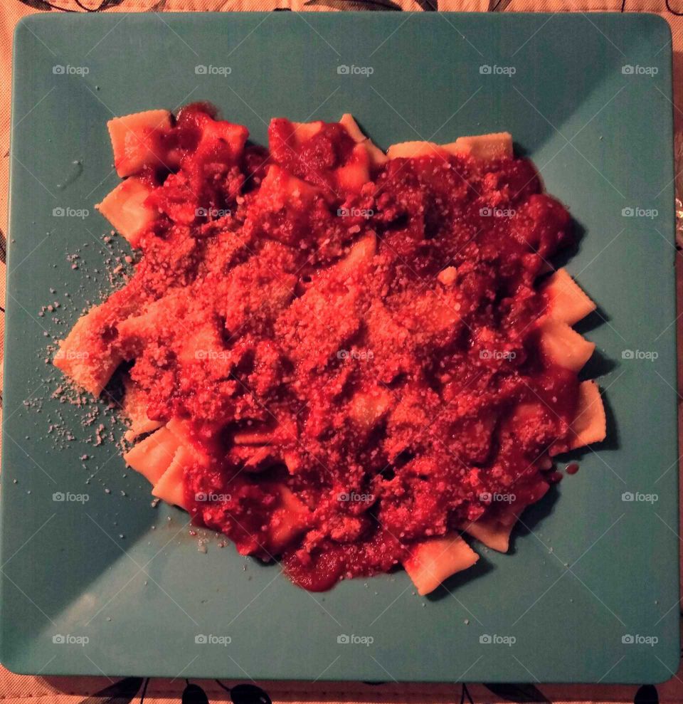 Dinner plate of mini ravioli with a meat & marinara sauce, and a sprinkling of parmesan cheese.