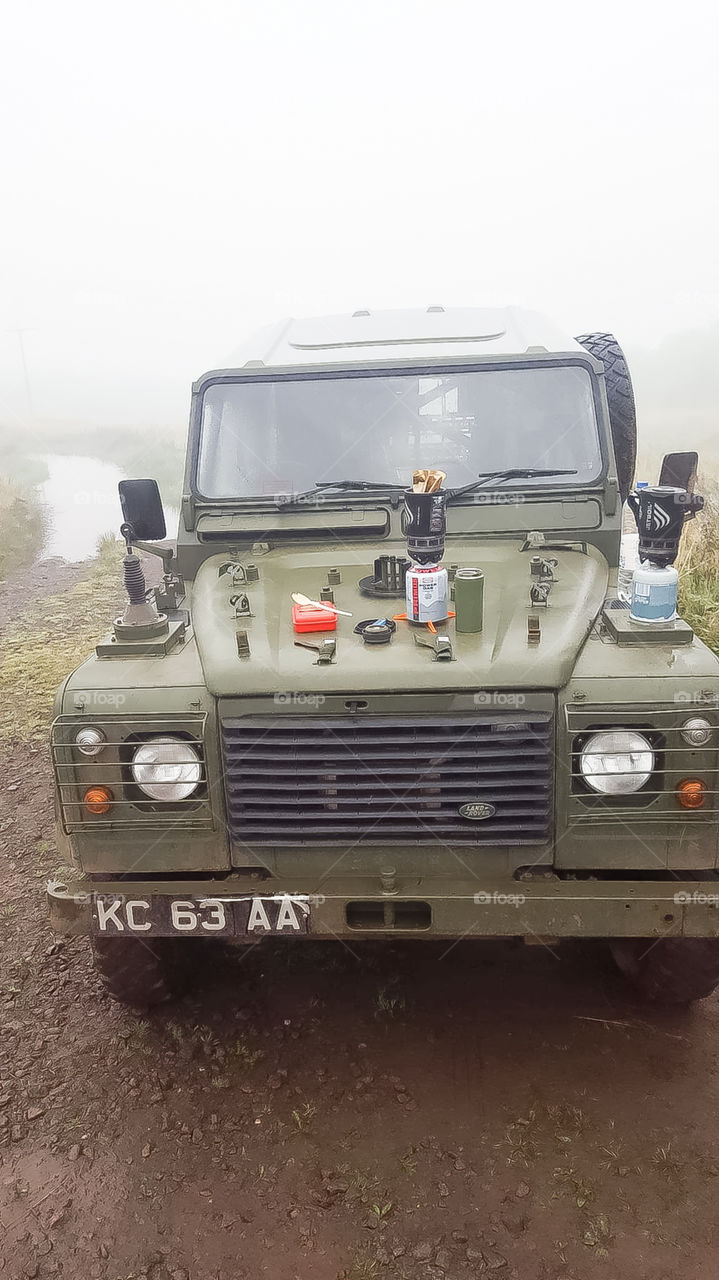 an army land rover sitting in the middle of a training area,as you can see the people driving the land rover are having a breakfast over a small site where a river is you can see the mist in the background