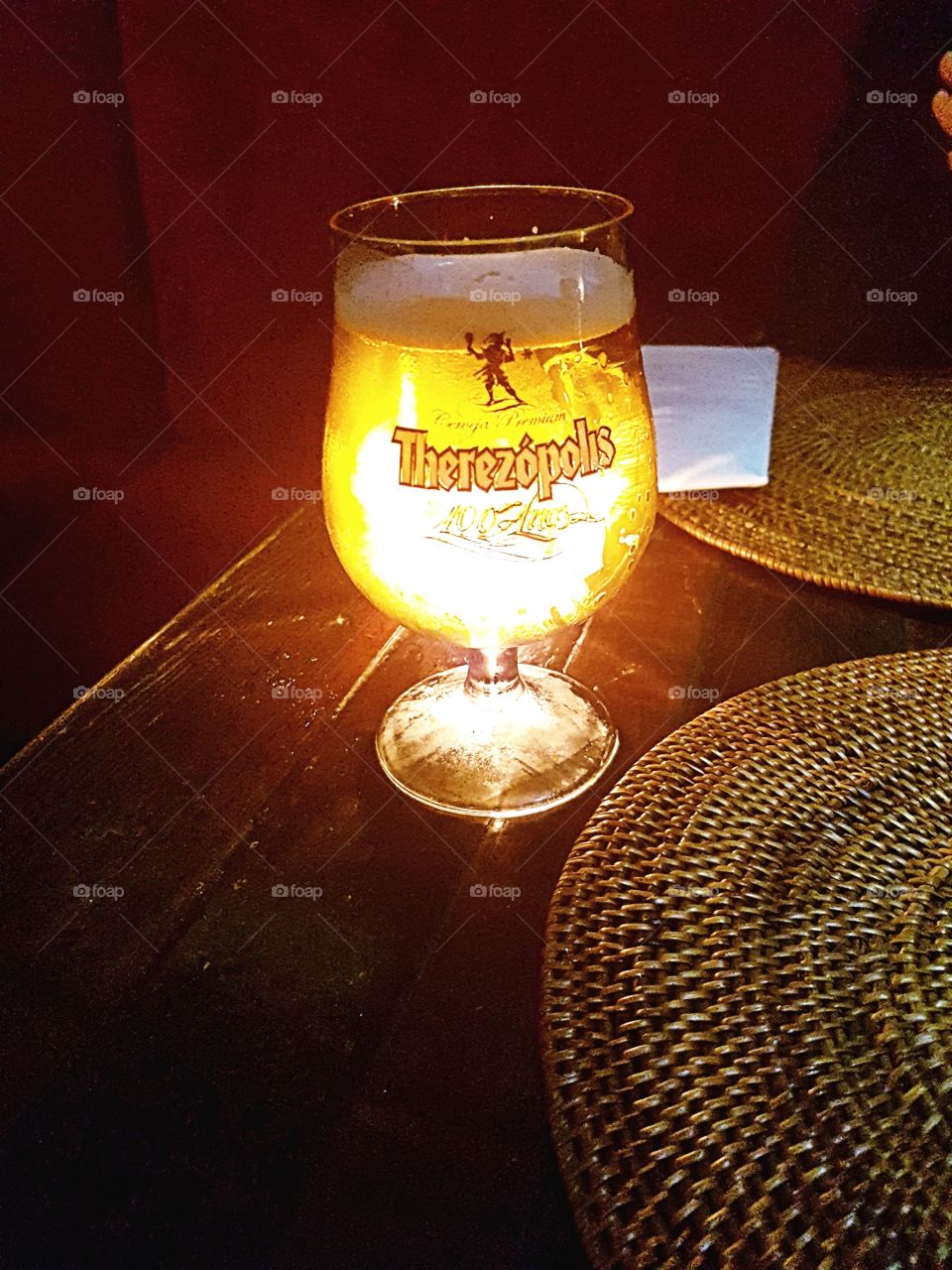 Just a beer and a candle on a table in a small restaurant.