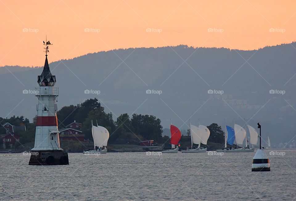 Regatta past a lighthouse in sunset