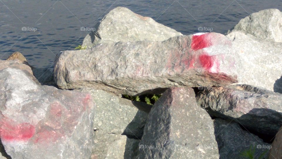 Riprap boulders marked with red paint splotches by the waterline at Shelter Island, San Diego, CA.