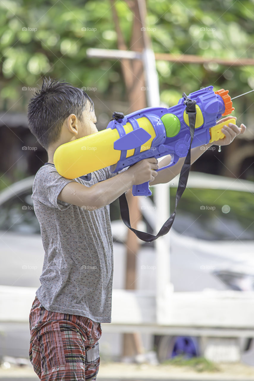 Asian boy holding a water gun play Songkran festival or Thai new year in Thailand.