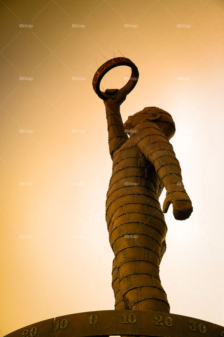 Metal sculpture of a man holding up a ring high towards the sky in a moment of triumph. Image acquired in a public park in the late afternoon sun.