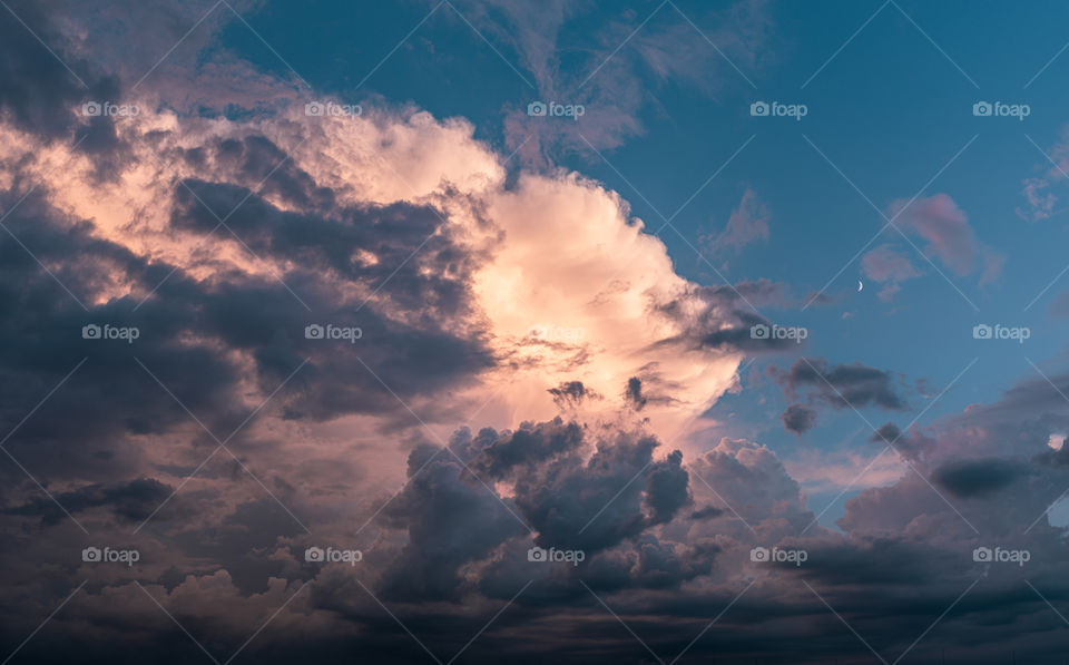 Dramatic glowing cloudscape with a crescent moon in the sky during mysterious sunset.