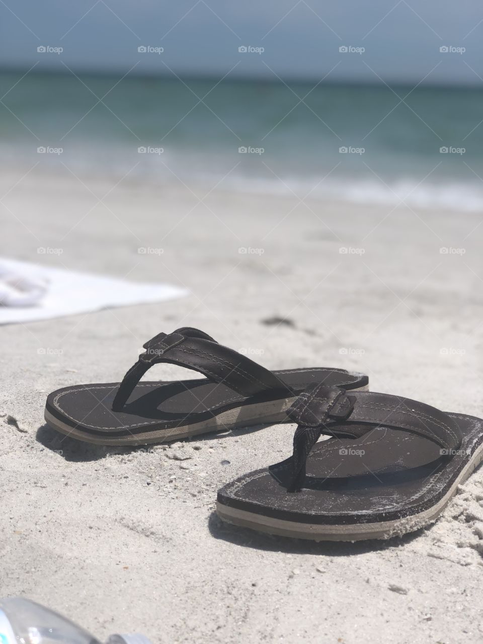 Flip Flops and towel laying in the sand on the beach. Waves crashing in the background. Summer beach day.
