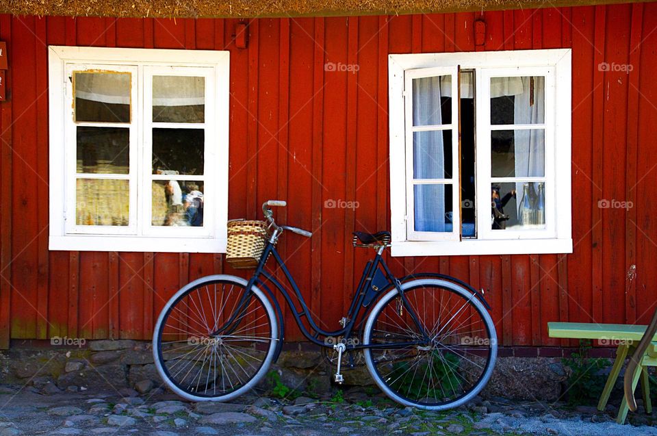 A classic bike is leaning at a red, wooden wall with two windows 