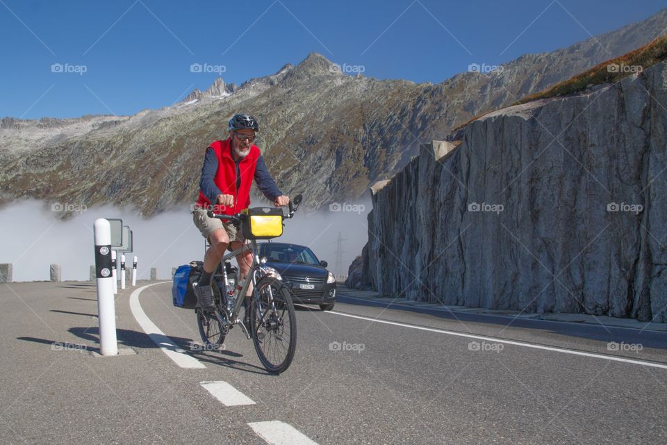 Old Man Riding His Bicycle Up A Road On The Swiss Alps