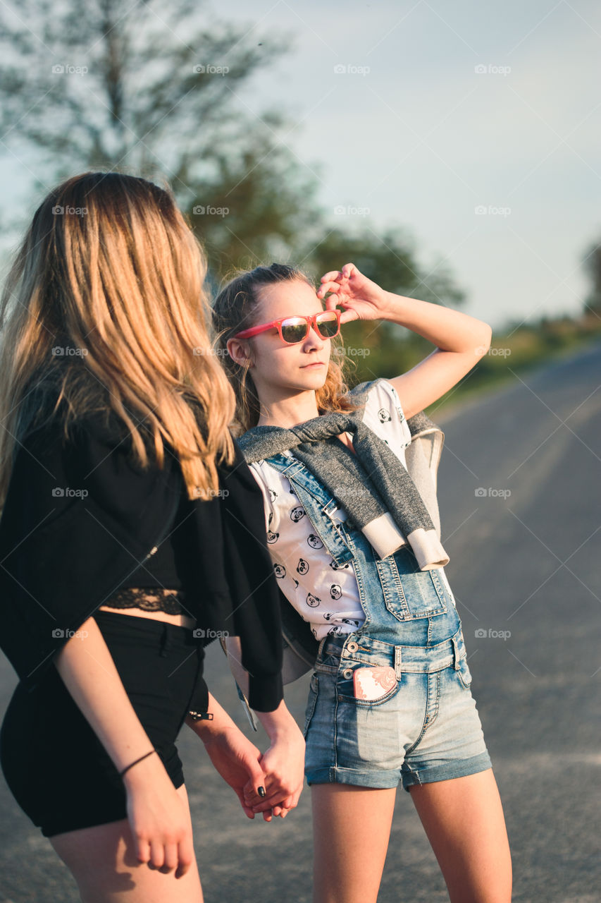 Teenage smiling happy girls having fun walking outdoors, hanging, spending time together on summer day. Real people, authentic situations