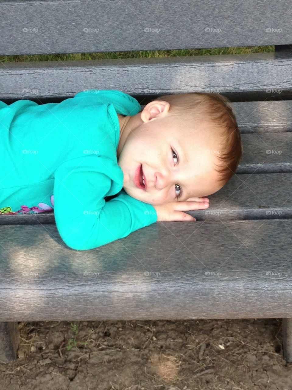 Ahhh. Toddler enjoying being outdoors lying on park bench