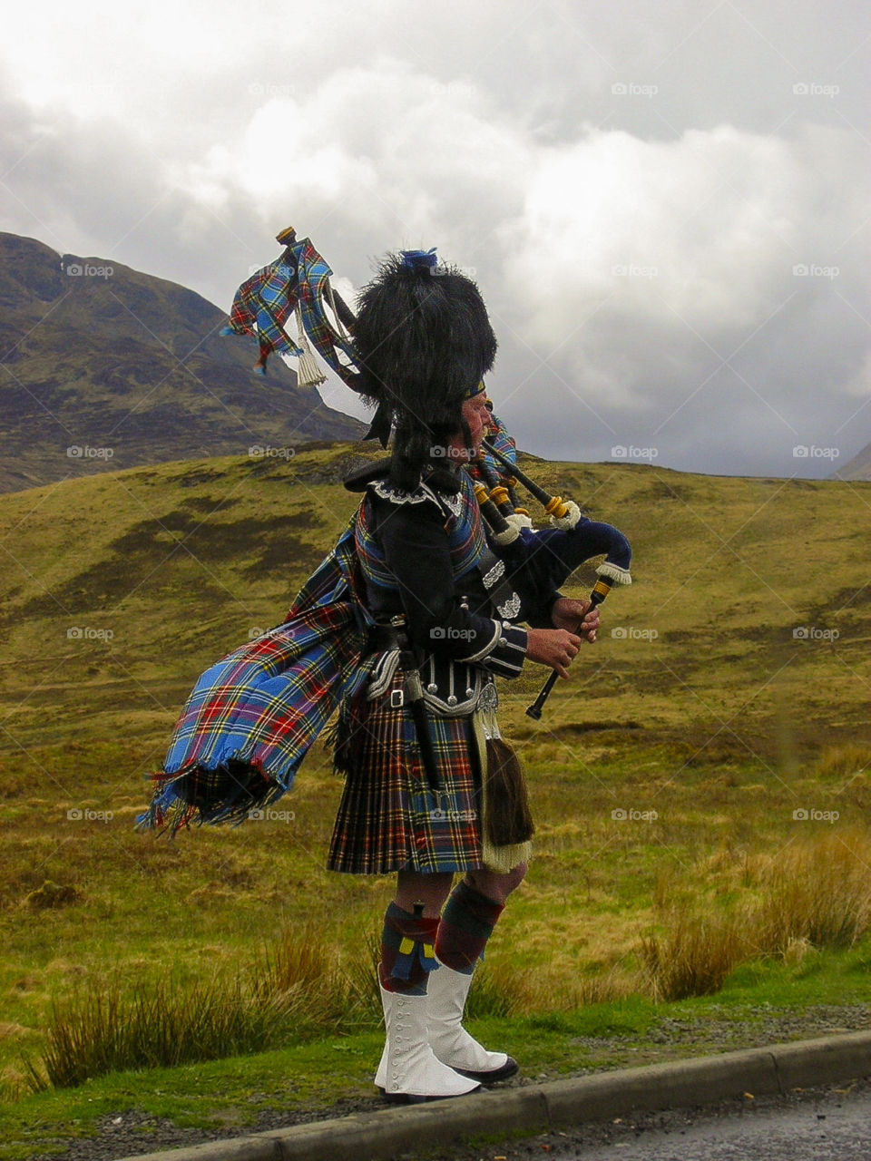 Scotland man playing bagpipes with kilt against mountain and fog 