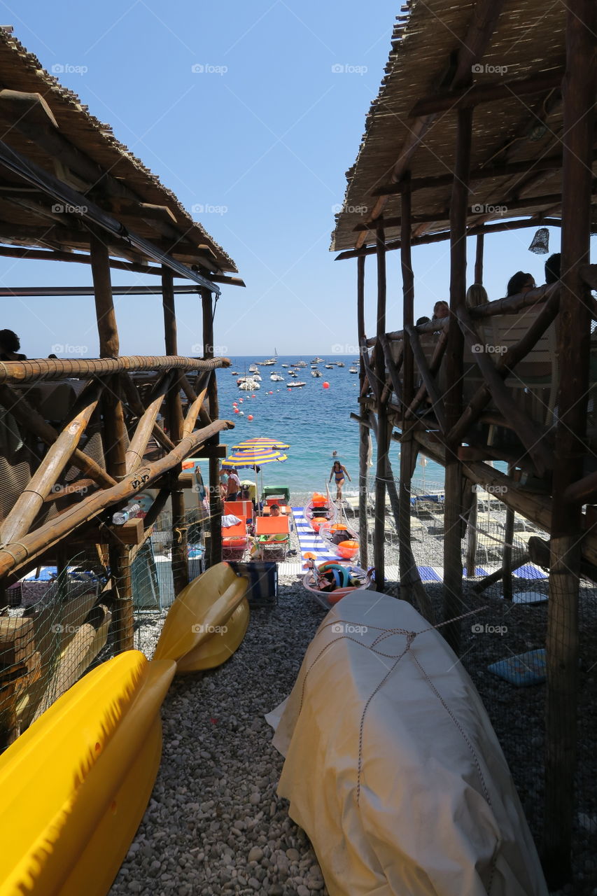 Beach shack restaurants on nerano beach italy. Looking out to sea , boats canoes people