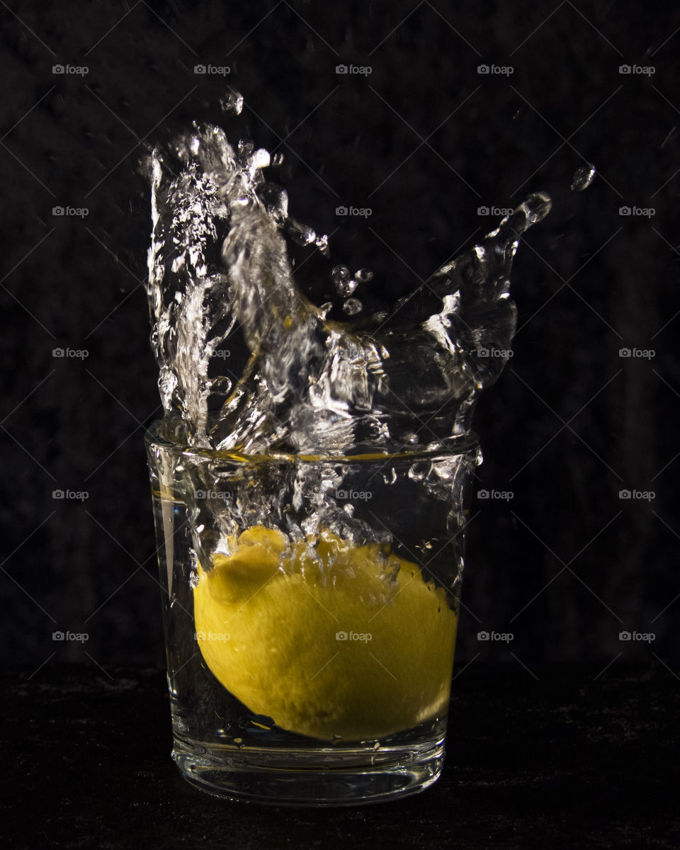 Fruit water splash, lemon dropped into glass full of water, black background 