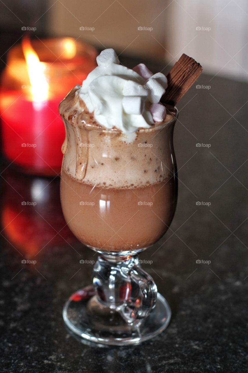 A hot chocolate in a glass coffee  cup with candles burning brightly.