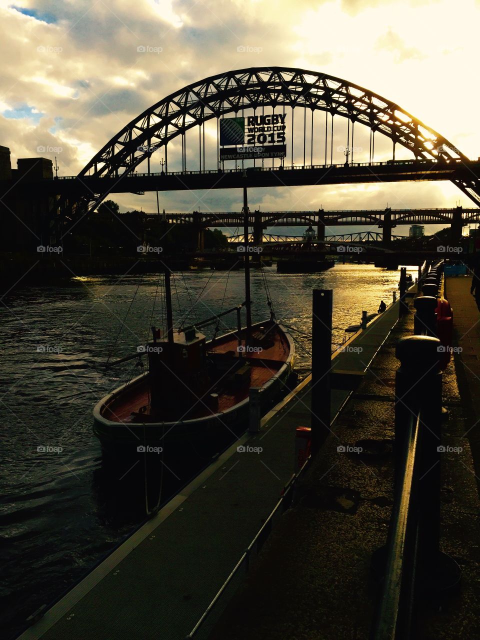 Newcastle Quayside at sunset. . The sun sets behind the Tyne Bridge and Rugby World Cup 2015 logo. 