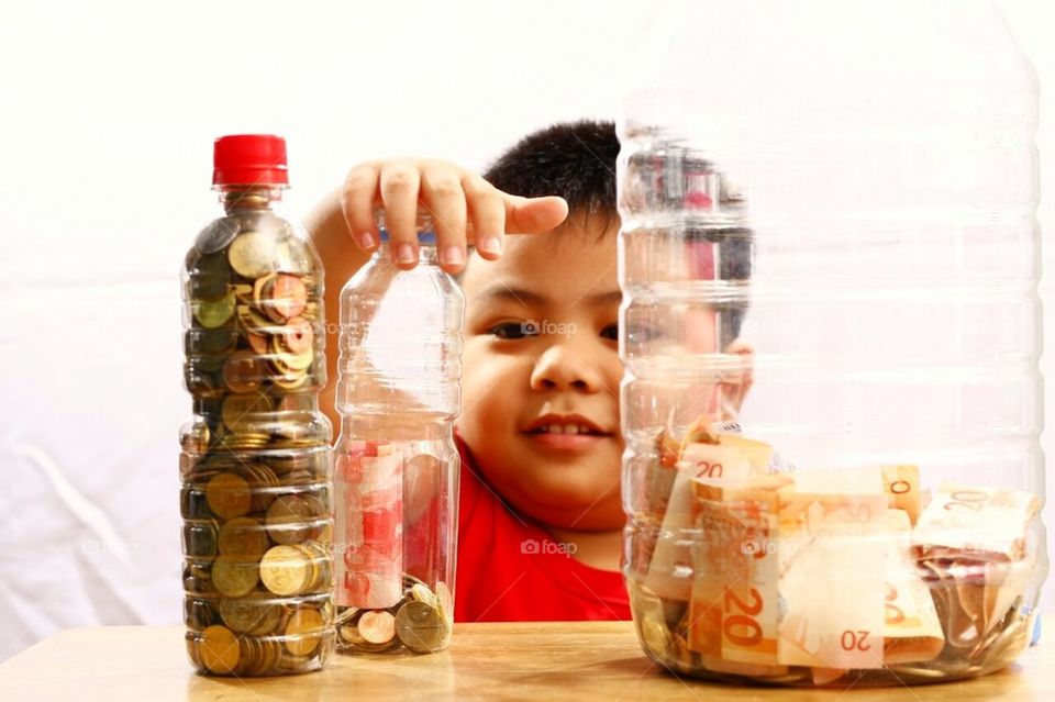 Little boy putting money in a bottle to save up