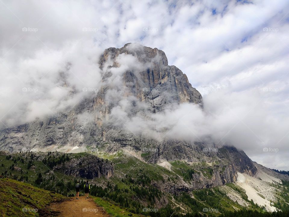 Hiking holiday in the Dolomites mountains. 2 hikers with big mountain in the clouds in background.