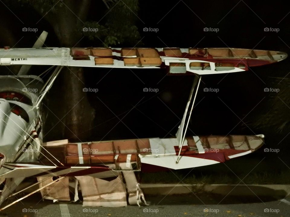 Broken left side wings from an old style private small white and brown plane in a parking lot in the evening at dawn in the dark.