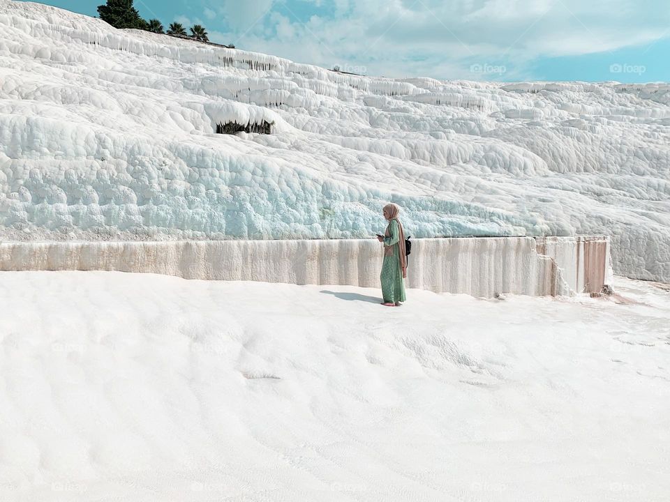 Young woman in green clothes standing on white chalk mountain with blue water 