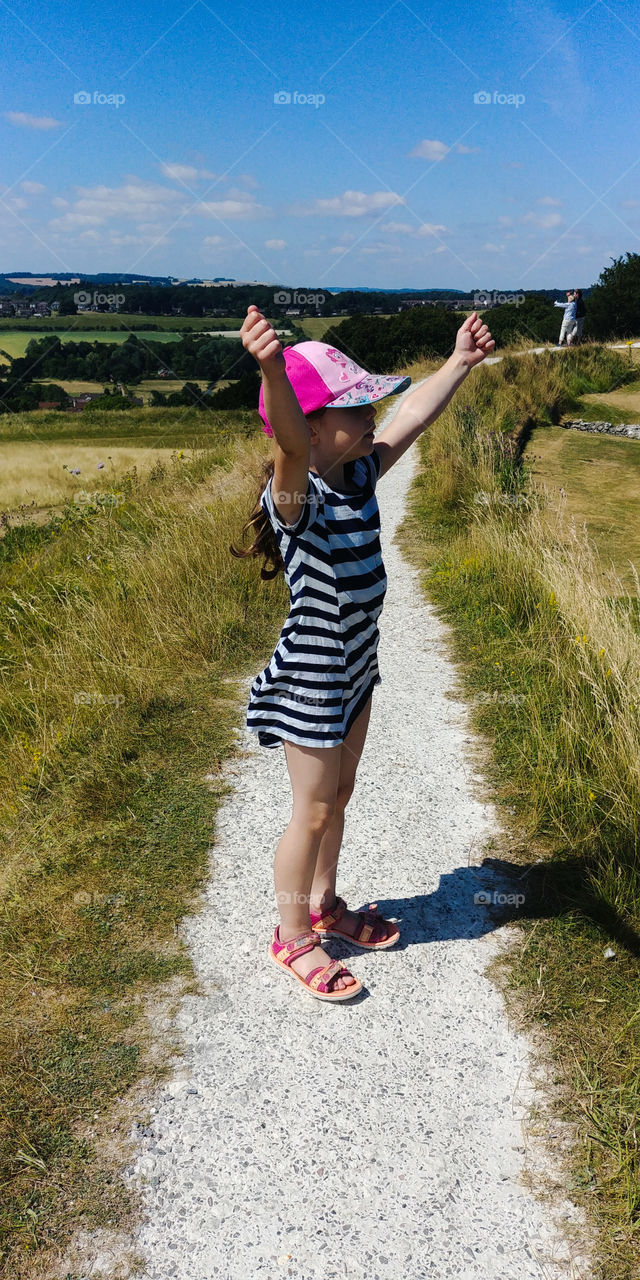 little girl in stripes dress on top of hill in summer with arms raised