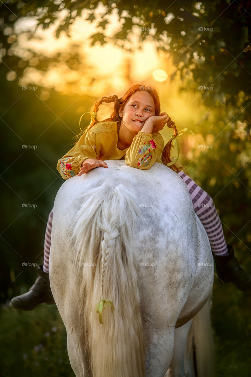 Funny red-haired girl portrait on grey horse, view from back 