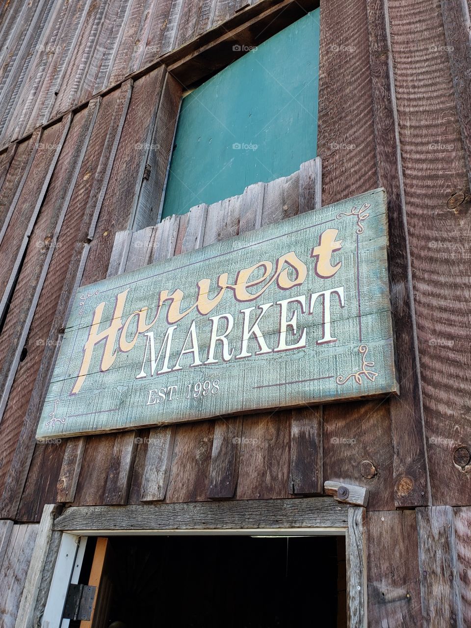 A sign for a farming harvest market made from weathered wood