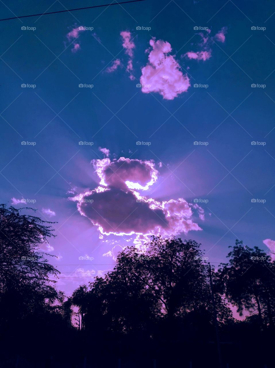 a shiney day just to before Sun set, sun shine behind the clouds, blue sky whitish cloud scattered dark tree looks very beautiful