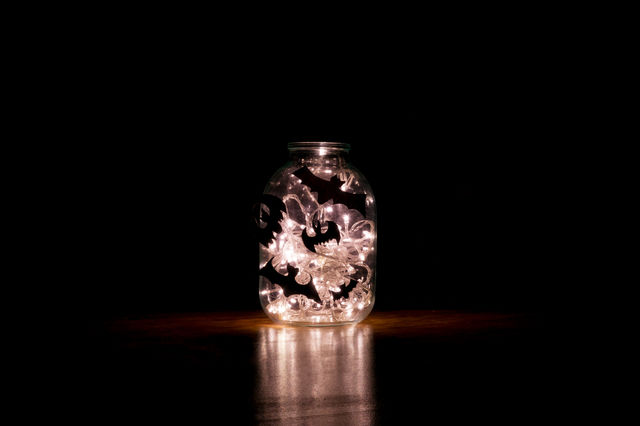 Halloween bats are glued to a glass jar with a garland glowing in it.