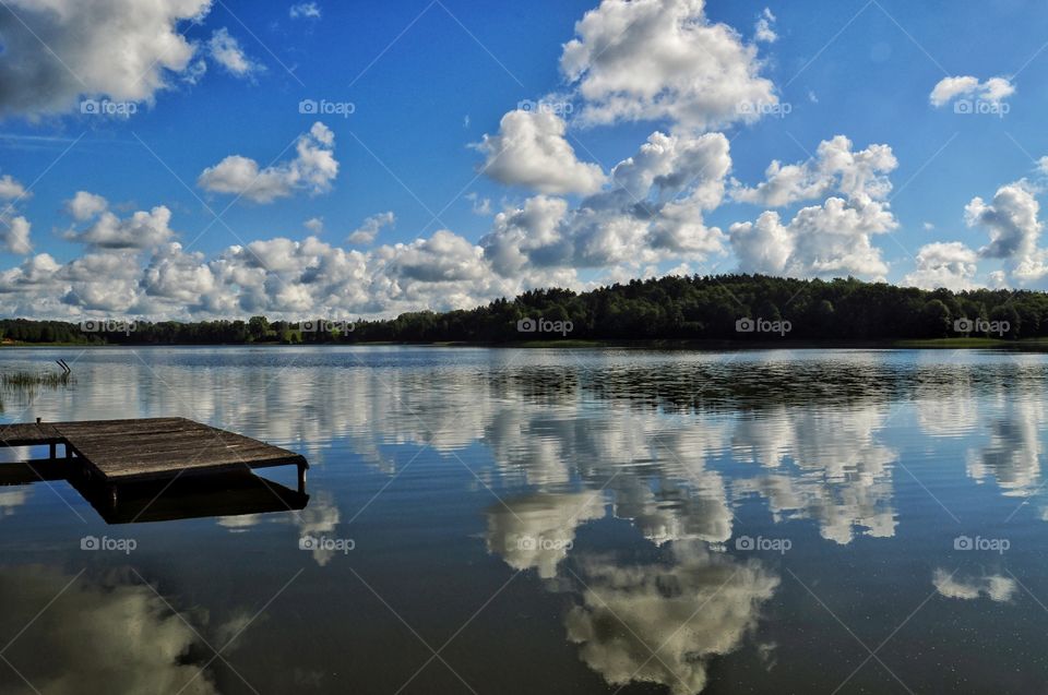 beautiful sunny day at the lake in polush countryside - forest on the horizon, wooden pier and blue cloudy sky