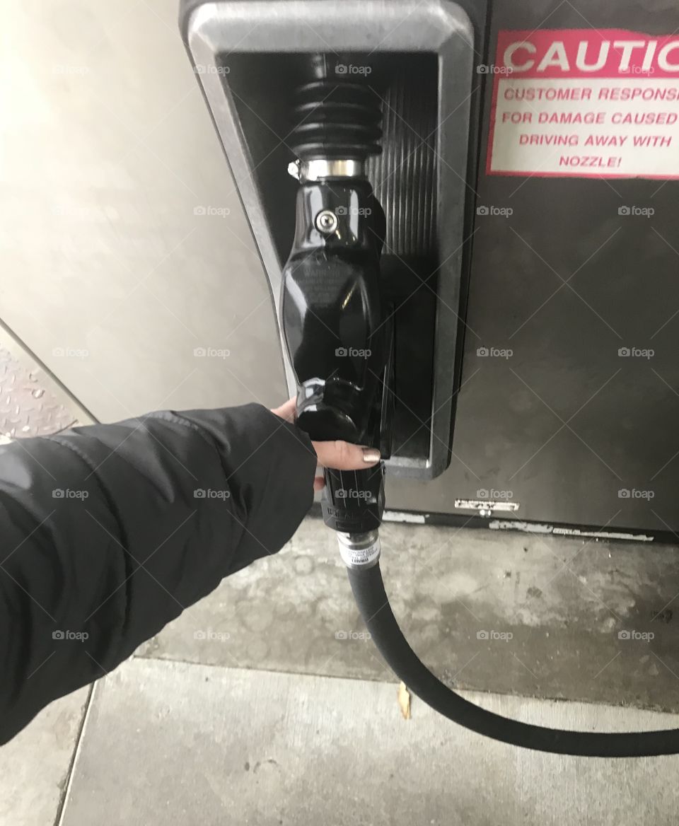 A lady wearing s coat on a cold winters day at the gas station ready to pump gas at the gas pump, located in USA, America. 