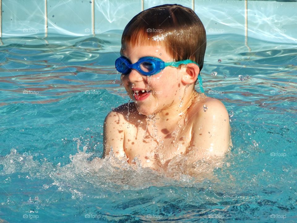 Happy Young Swimmer. Young Boy Splashing Happily In A California Swimming Pool
