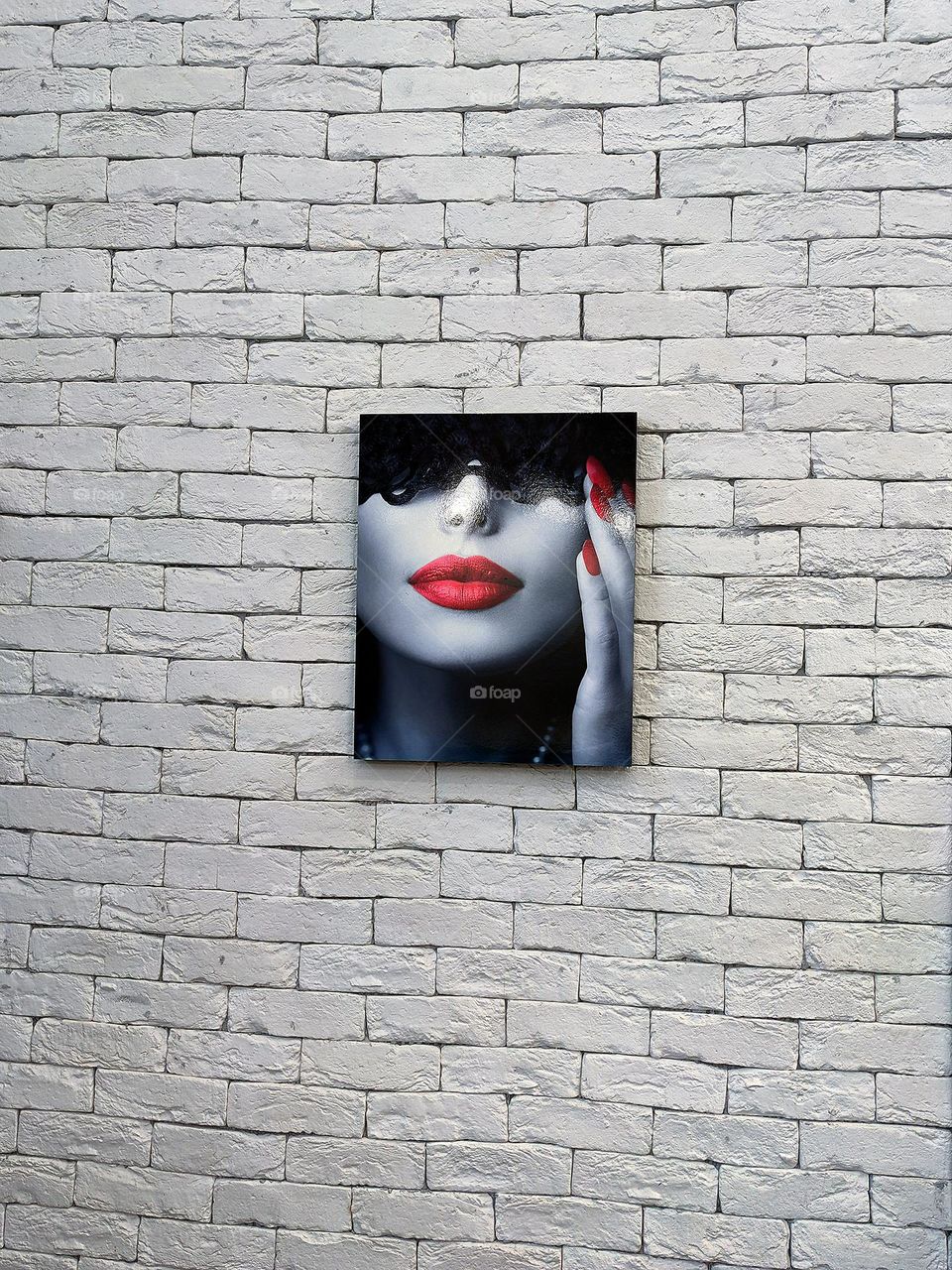 The minimalism of the object. A multi-colored black and red portrait of a girl hangs on a white brick wall. Background and subject contrast