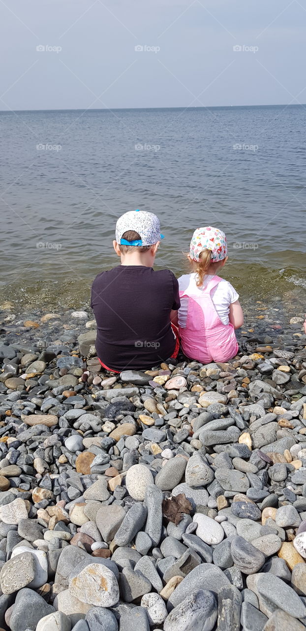 Brother and sister sitting by the sea at high tide