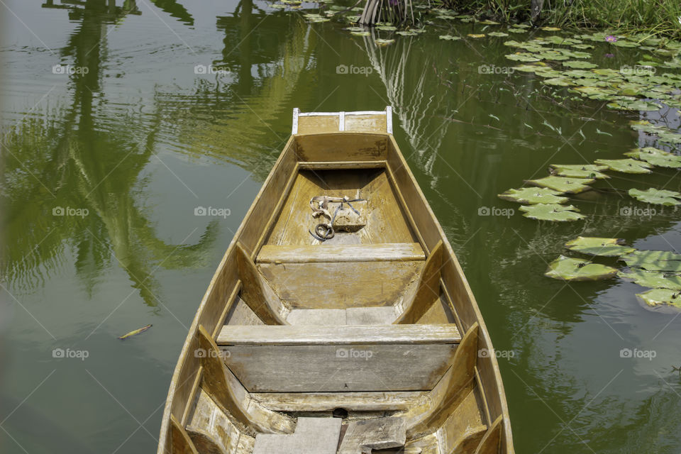 The boat made of wood floating on the water in the lotus pond.