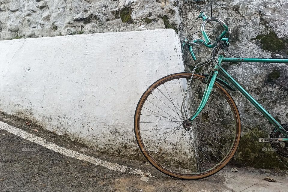 a dark green bicycle parked against a rough white and gray wall