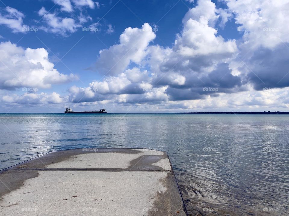 Cargo ship on horizon Lake Huron at Port Huron, Michigan on partly cloudy day, billowy clouds, vantage from concrete dock onshore facing Canada