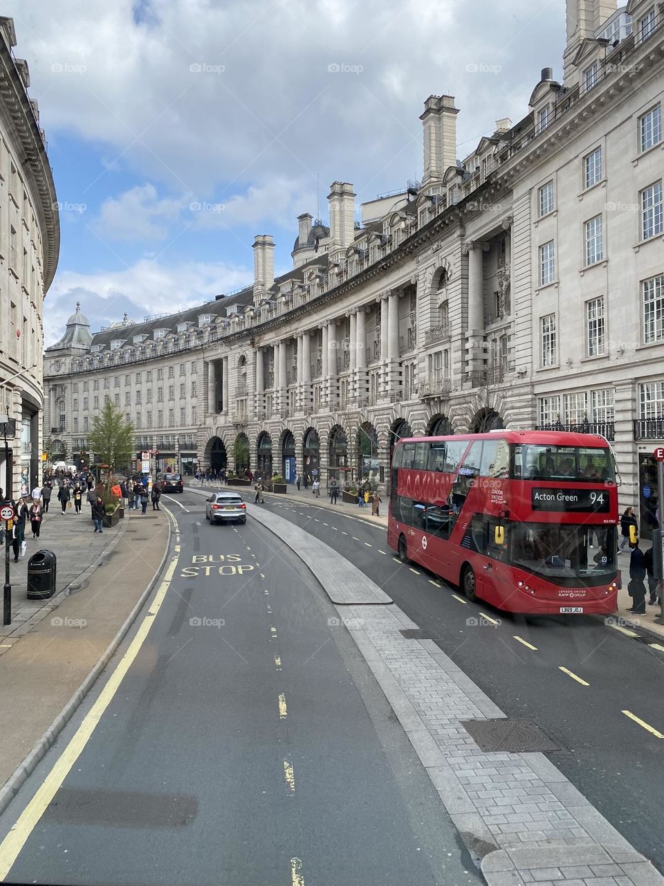 Red London bus with double decker circulating in Regent street between typical white buildings.